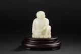 A CARVED WHITE JADE FIGURE OF SEATED BOY