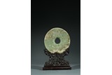 A CHINESE CELADON JADE DISC WITH HARDWOOD STAND